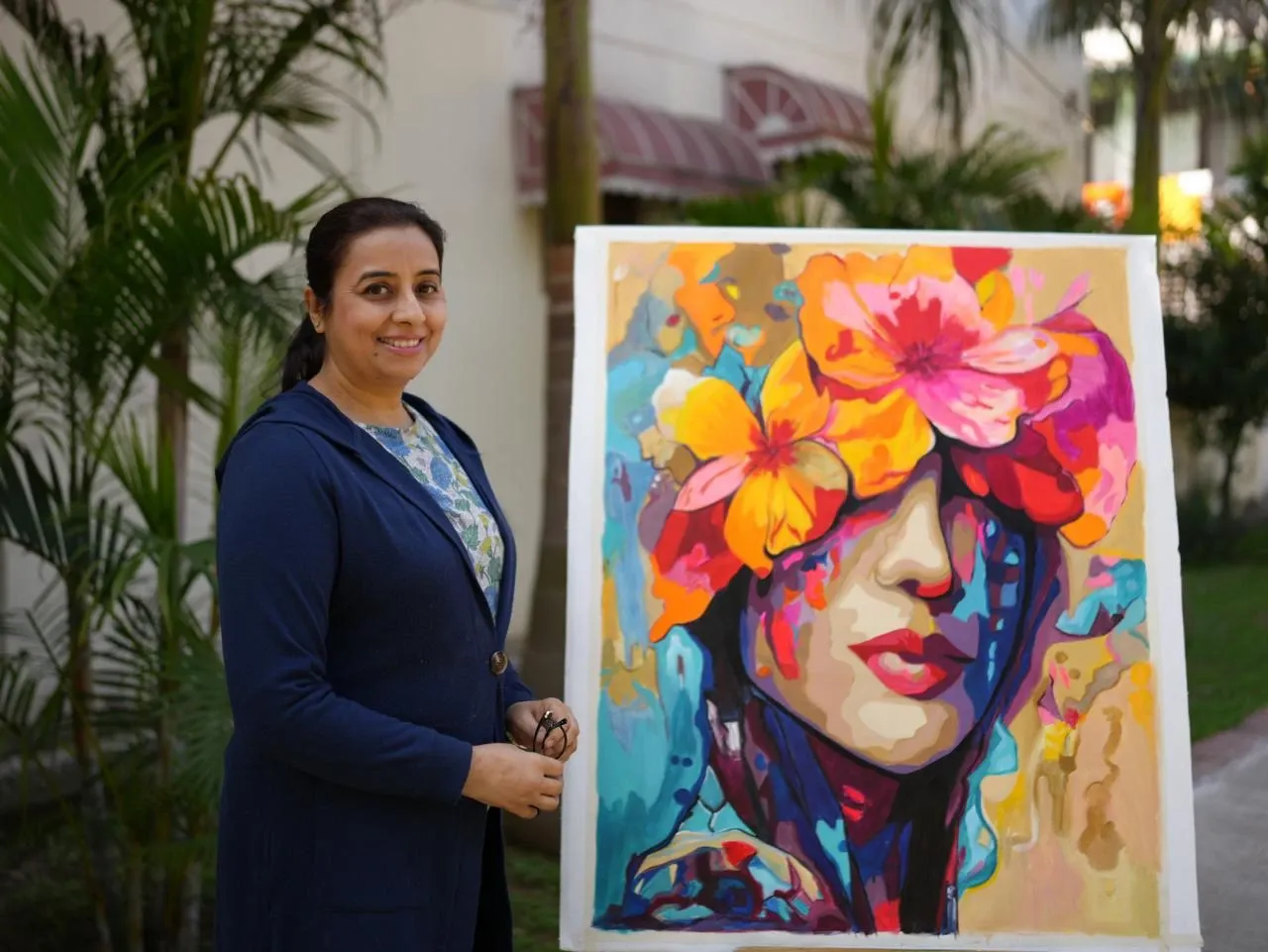 Balpreet Kaur beside one of her paintings: a woman's face crowned with orange and pink flowers