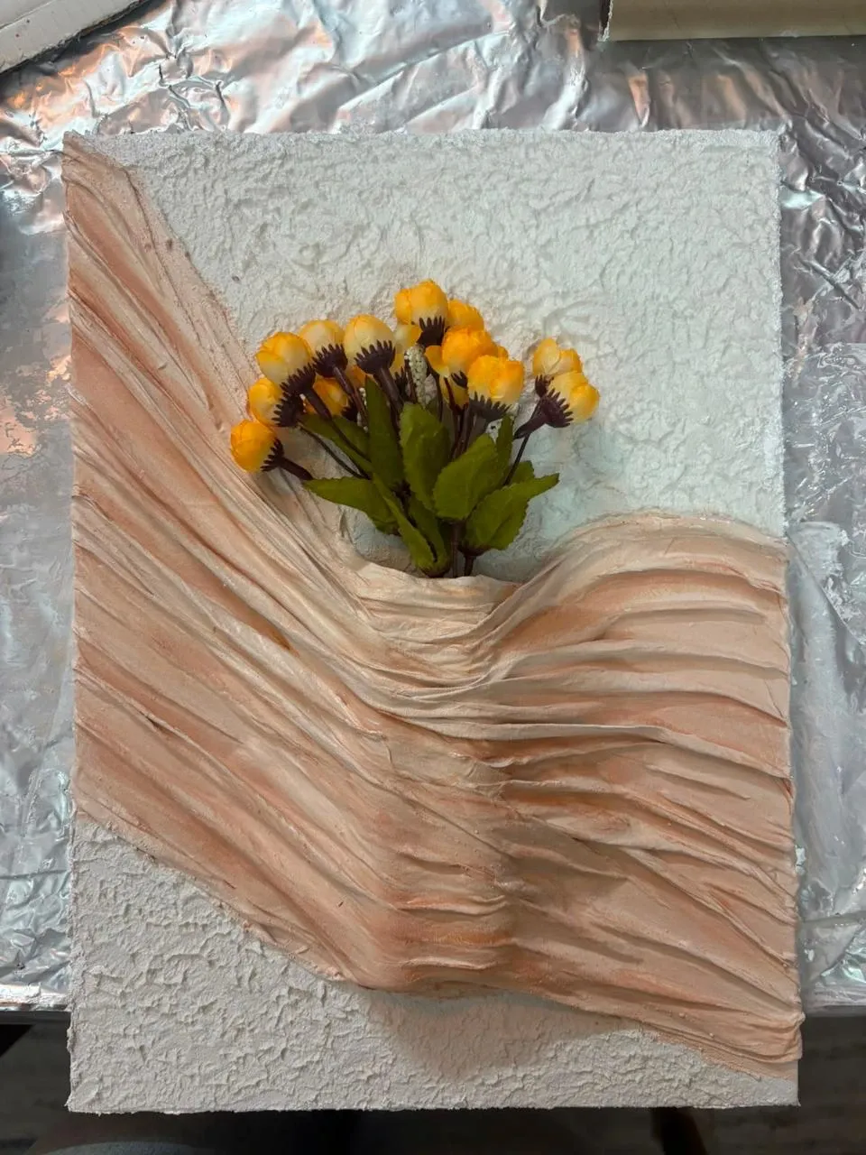 A textured canvas with draped cloth in peach holding a bunch of yellow flowers